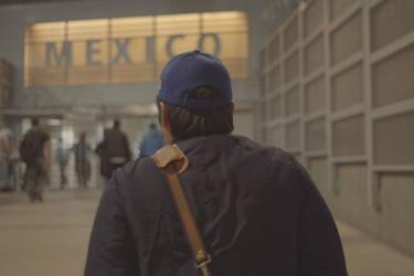 Person with blue baseball hat and brown shoulder strap is facing a sign that reads Mexico inside of an airport