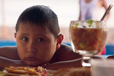 Still from Sanson and Me, young boy resting their face on their hands behind a bowl of food