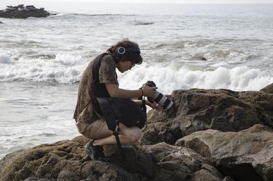 Chisa Hughes on rocks by ocean with camera